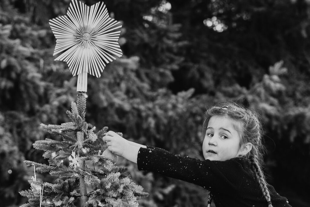 Kind steckt Stern auf Weihnachtsbaum in Schwarz/Weiß